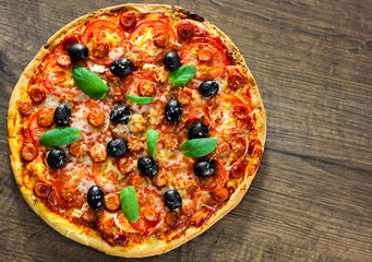 Pizza with Mozzarella cheese, salami, pepper, pepperoni, Tomatoes, olives, Spices and Fresh Basil. Italian pizza on wooden background. with copy space. top view