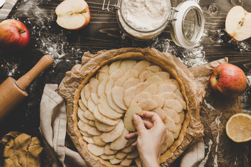 Cooking apple pie. Hands adding apple slices to pie crust. Apple pie ingredients on wooden table