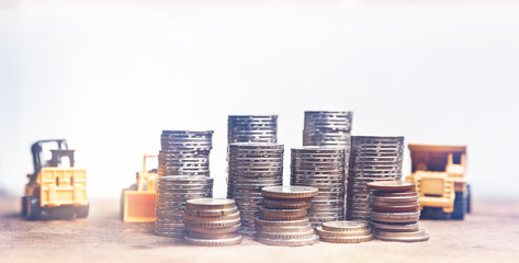 Financial And Macro Economic Concept, pile of coins money stacked on wooden table, with construction vehicle and equipment. Vintage tone.