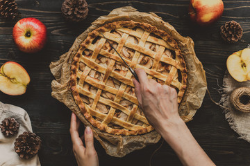 Hands cutting homemade delicious apple pie on the wooden rustic table. Top view