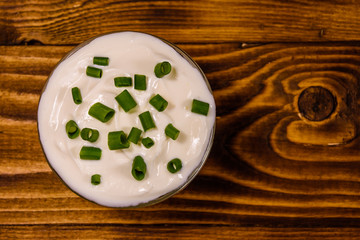 Glass bowl with sour cream and chopped green onion on wooden table. Top view