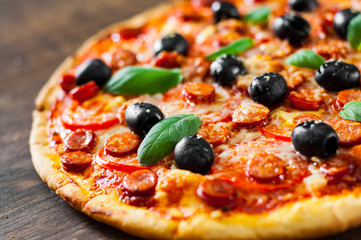 Pizza with Mozzarella cheese, salami, pepper, pepperoni, Tomatoes, olives, Spices and Fresh Basil. Italian pizza on wooden background