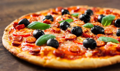 Pizza with Mozzarella cheese, salami, pepper, pepperoni, Tomatoes, olives, Spices and Fresh Basil. Italian pizza on wooden background