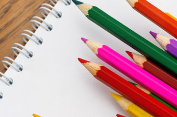 White paper and colored pencils lie on a wooden table