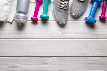 Sport and fitness symbols - sneakers, water, towel and dumbbell on wooden wall background