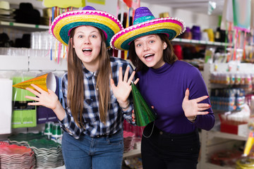 Attractive girls trying on party hats in festive accessories shop
