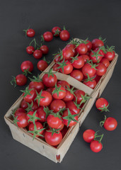 Small red cherry tomatoes in a wicker rattan basket on a wooden black background in rustic style, selective focus. red tomatoes. full view from above.