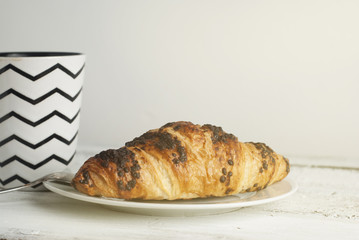 Cup of coffee with croissant on a white plate over white table Breakfast, selective focus, toned. Copy space for text.