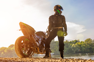 Man wearing motorcycle helmet and safety uniform sitting on bike outdoors, beautiful scenic...