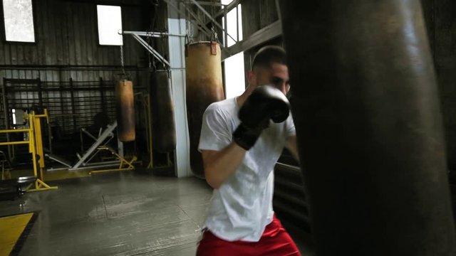 Handsome young male training with punching bag in the gym. Hardworking boxer effectively working on her punches with some aggression. Close up