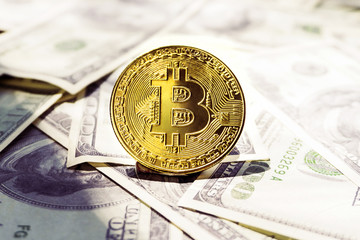 Gold bitcoins laying over the hundred dollar bills