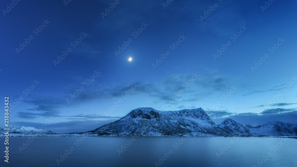 Wall mural snow covered mountains against blue sky with clouds and moon in winter at night in lofoten islands, 