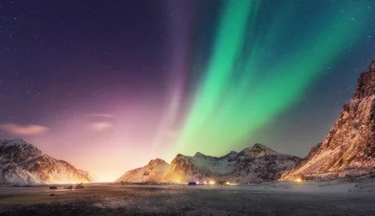Poster Green and purple aurora borealis over snowy mountains. Northern lights in Lofoten islands, Norway. Starry sky with polar lights. Night winter landscape with aurora, high rocks, beach. Travel. Nature © den-belitsky