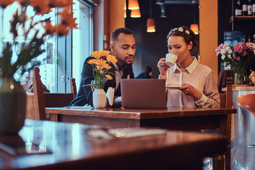 Attractive African-American couple at a business meeting in the restaurant discussing working moments with laptop at lunchtime.