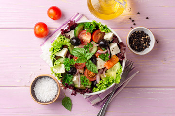 Fresh Greek salad with vegetables, feta cheese and black olives in white bowl on purple wooden background