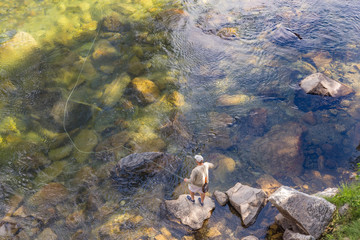 A Man Fly Fishing in a Shady Rock-Filled River