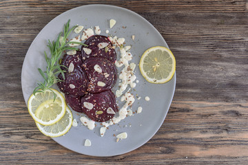 Baked beet sliced in slices in a plate next to a branch of rosemary and slices of lemon (top view)
