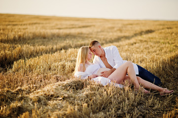 Naklejka na ściany i meble Pregnant couple in wreath field at white underwear clothes on sunset. Happy moments of pregnancy.