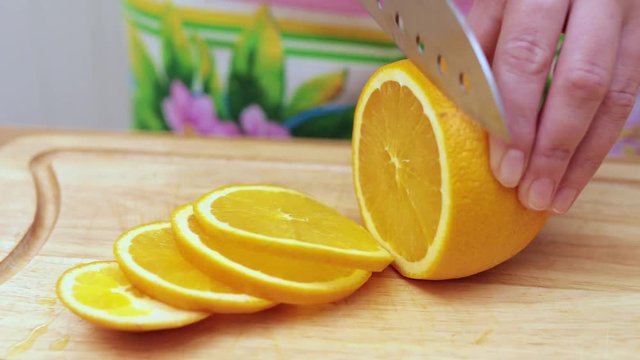 Women's hands Housewives cut with a knife fresh orange on the cutting Board of the kitchen table