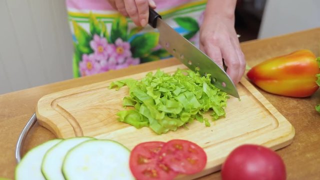 Female hands of housewife with a knife cut fresh lettuce on a chopping Board kitchen table