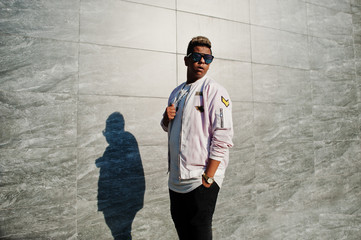 Stylish hipster arab man guy in sunglasses posed outdoor in street at sunset against gray wall.