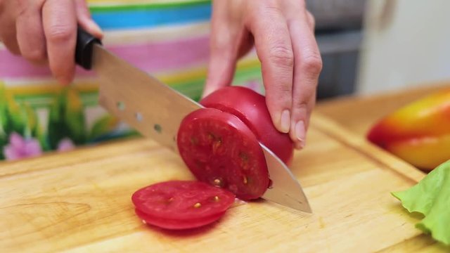Women's hands Housewives cut with a knife fresh tomato on the cutting Board of the kitchen table