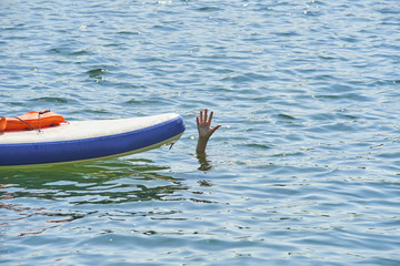 Hand of a drowning child boy leaning out of the water beside the paddleboard