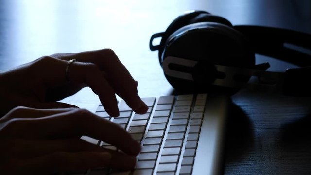 Woman's hands are putting headphones and typing on the keyboard 