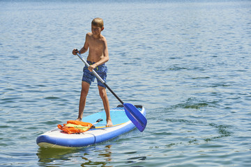 Paddle boarder. Child boy paddling on stand up paddleboard. Healthy lifestyle. Water sport, SUP surfing tour in adventure camp on active family summer beach vacation.