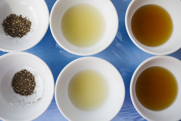 Assortment of basic food flavoring and seasoning ingredients ready for cooking. Ground Black Pepper, Lime Juice and Fish Sauce in separate bowls on blue table. Close up. Natural light.
