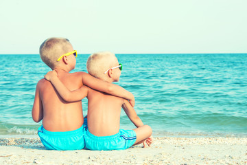 Two brothers relaxing on the beach,sitting on the sand and looking at the sea. Summer vacations.	