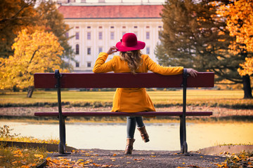 Attractive young woman with red hat sitting on a bench in park and enjoying a view on castle at...