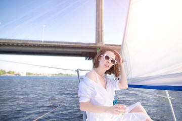 Portrait of a beautiful woman sailing on a yacht along the river, posing with a glass of wine in her hands against the background of the river and the bridge.Woman walk on a yacht with a glass of wine