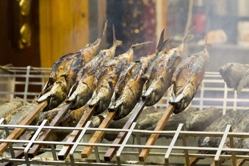 Barbecue stockfish grilled trout fish on stocks with fire smoke. Delicious crispy staple nutrition...