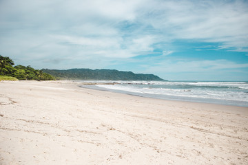 Obraz premium Clean sandy beach of Santa Teresa, Puntaarenas province in Costa Rica on a hot summer's day with blue skies and few tourists
