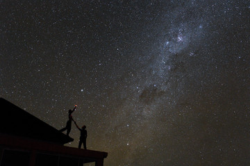 Fototapeta na wymiar Couple on rooftop watching mliky way and catching stars in the night sky on Bali island