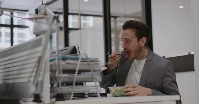 Adult male having lunch whilst working at desk in office