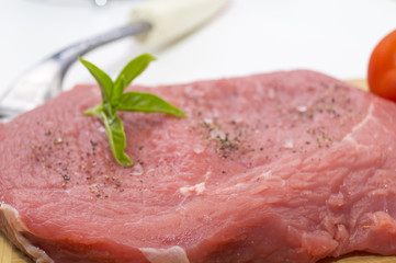 raw beef steak on cutting board with cherry tomatoes and basil leaf