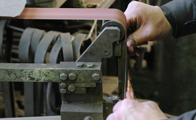 Grinding billets of metal knife on a belt-grinding machine. Close-up of a man's hand.