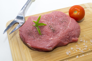 raw beef steak on cutting board with cherry tomatoes and basil leaf