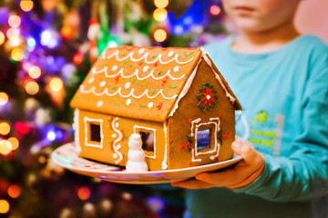 Christmas gingerbread house in children's hands close-up against the backdrop of lights in the...