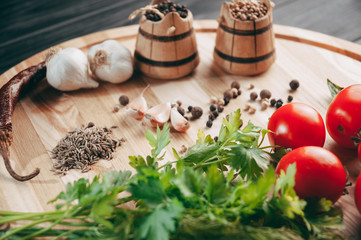 Spices: chili, black pepper, garlic, cumin, coriander, sweet pepper lie on a brown round wooden board on a black table. Place under the text.
