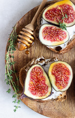 Mini bruschetta (toast or sandwich) with ricotta (cream cheese), fig, honey and thyme served on wooden rustic plate. Healthy food concept. 