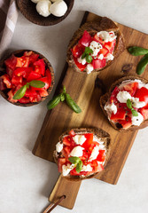 Italian bruschetta with chopped cherry tomatoes, mozzarella cheese and basil on wooden cutting board. 