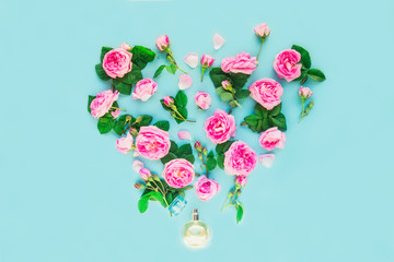 Fototapeta premium Close up creative layout with Perfume bottle and pink tea rose flowers in shape of heart on the blue background. Fresh concept with luxury aroma perfume. Beauty cosmetic. Selective focus. Copy space.