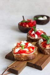 Italian bruschetta with chopped cherry tomatoes, mozzarella cheese and basil on wooden cutting board. 