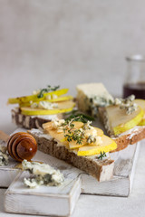 Toast or bruschetta with ricotta or cream cheese, pear, honey and blue cheese on white wooden cutting board. Delicious breakfast or snack on a light background.