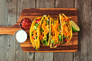 Hard shelled tacos with ground beef, lettuce, tomatoes and cheese. Above view on an old wood background.