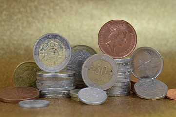 stacks of coins from different nations with Euros and Cents in front of golden background