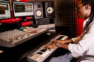 African man playing on synthesizer in recording Studio